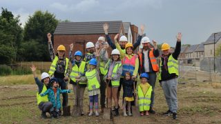 group of people standing on a site waving in hard hats